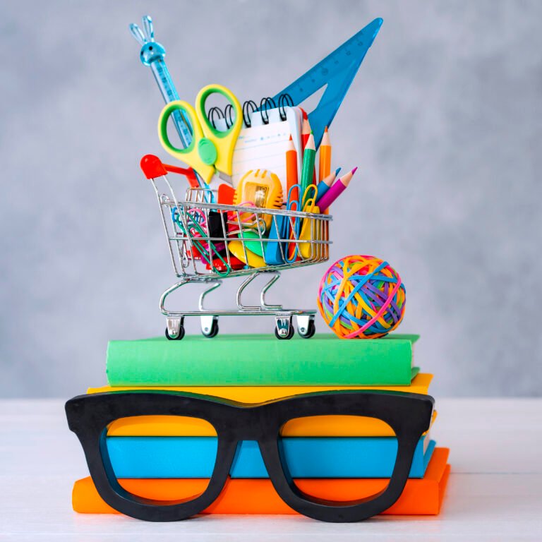 Colorful school supplies shopping basket gray background with a copy text space. A stack of books with colorful covers frame glasses. Colorful school supplies shopping basket gray background with a copy text space. A stack of books with colorful covers frame glasses.